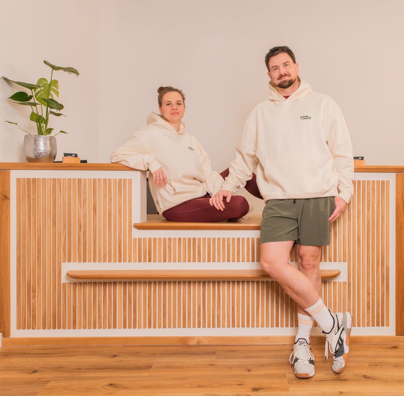 Anne und Mitja Langholz – Move and Mind Therapie Harburg Anne sitzt auf und Mitja lehnt am Praxis-Empfangstresen