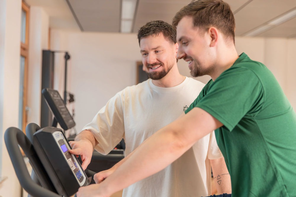 Individuelles-Fitnesstraining-Harburg-Move-and-Mind Mitja erklärt männlichem Patienten den Crosstrainer