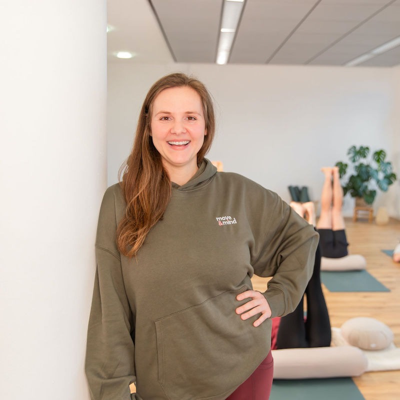 Lächelnde Anne mit Yogateilnehmern in Rückenlage im Hintergrund